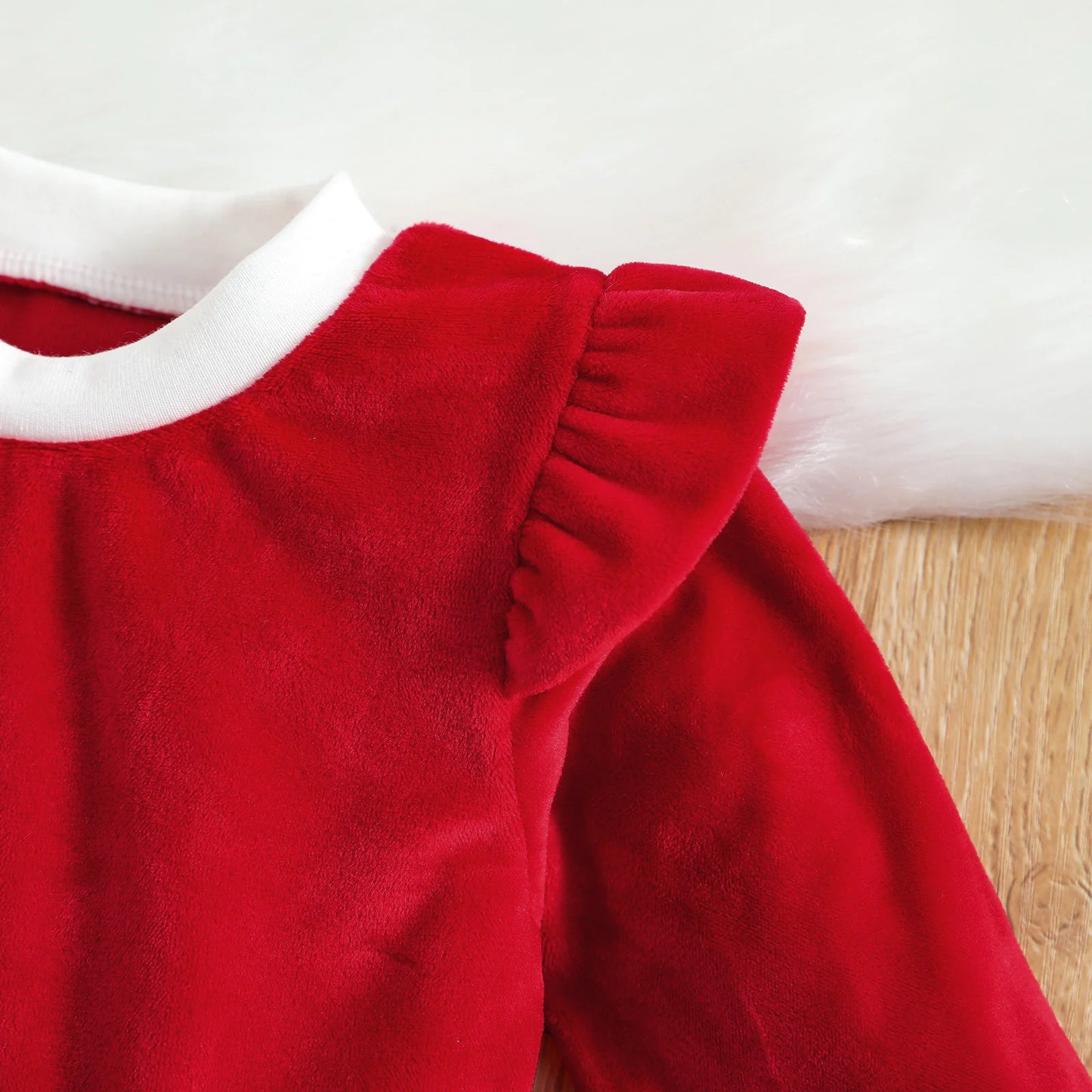 Close-up of neckline and ruffle shoulder design on red velvet baby Christmas outfit.