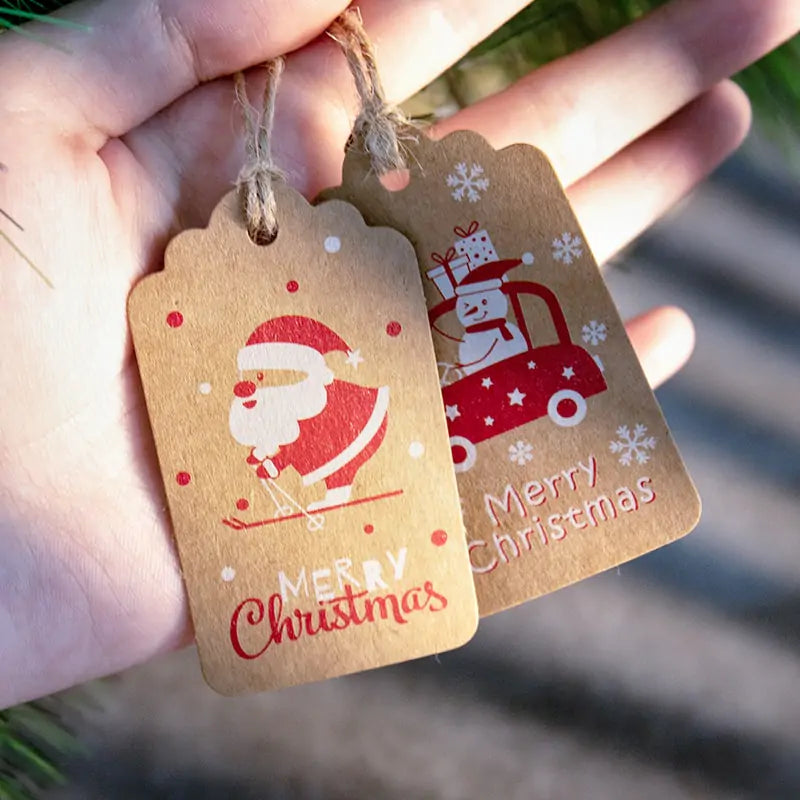 Velaflare Santa and snowman kraft gift tag held in hand with attached hemp twine, showing real size.