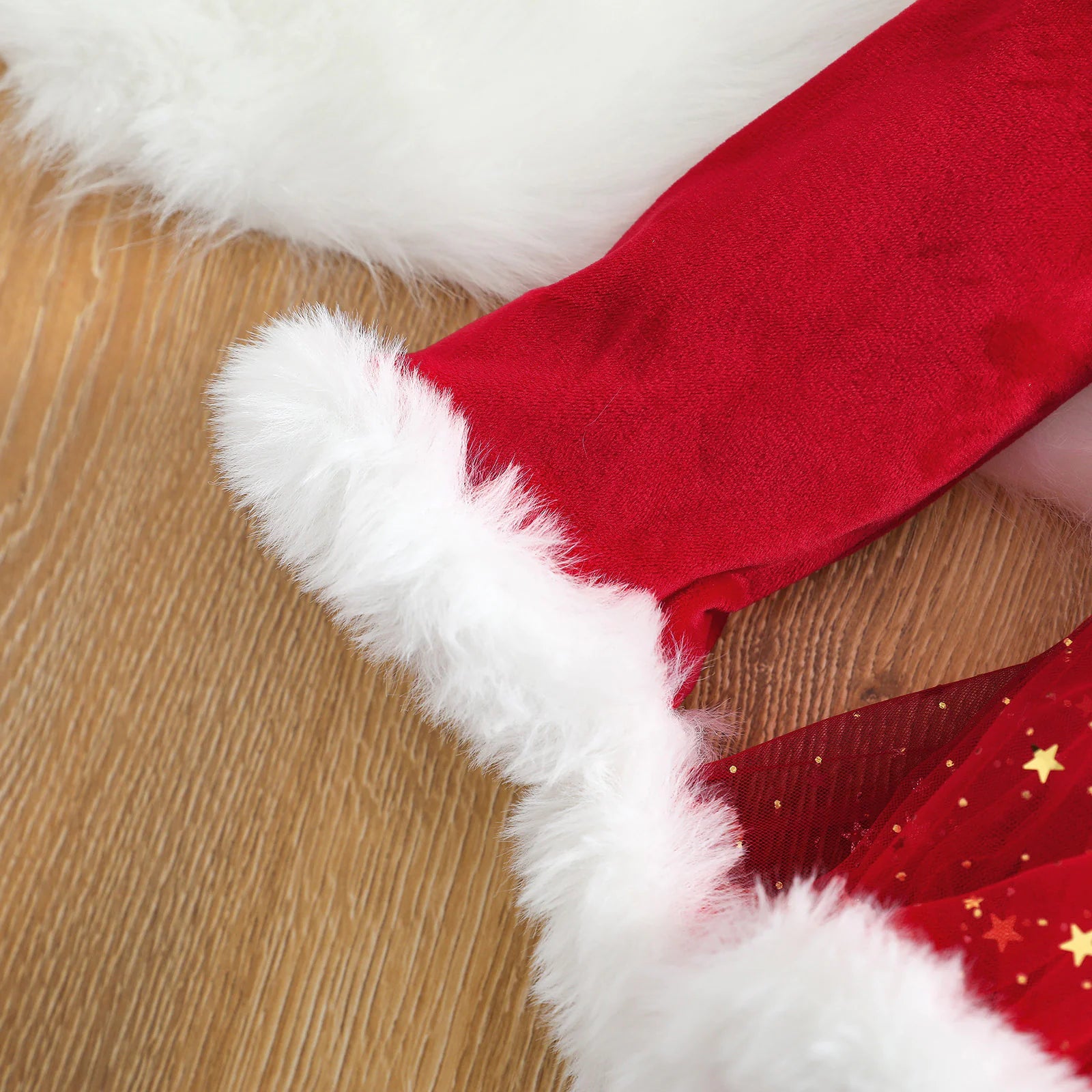Close-up of red velvet sleeve and white fur trim from baby Christmas romper showing fabric texture.